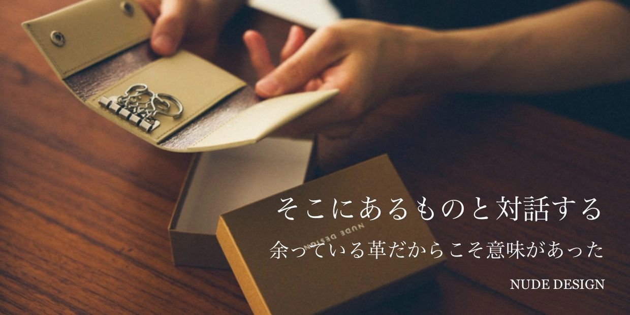 Hands holding a leather key holder with a box on a wooden table, featuring Japanese text.