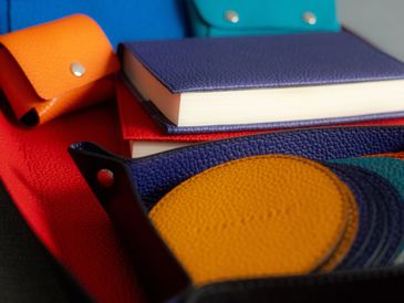Colorful leather accessories including wallets, coasters, and a notebook cover.