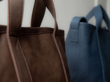 Close-up of brown and blue leather tote bags hanging.