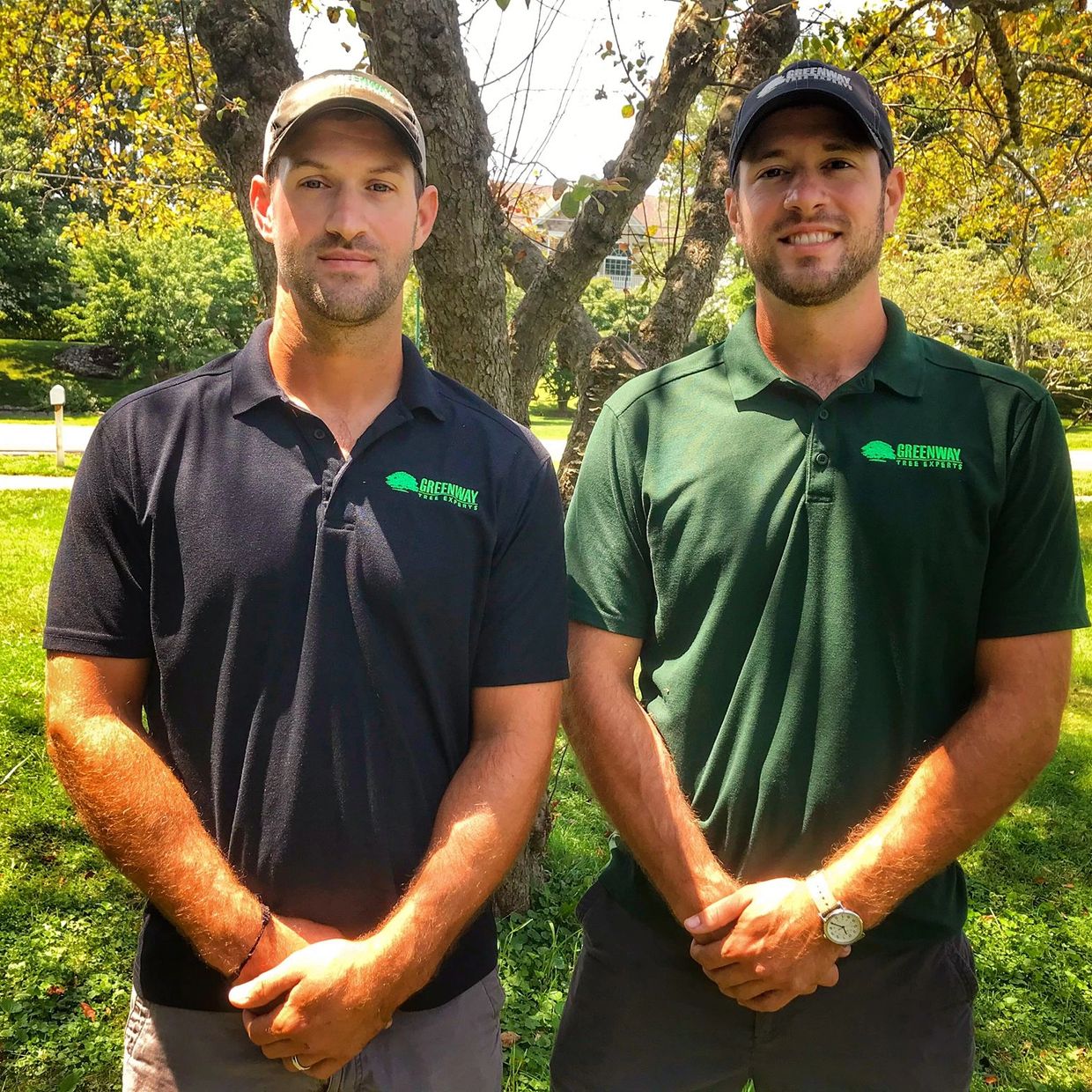 Two men in Greenway Tree Experts shirts standing outdoors.
