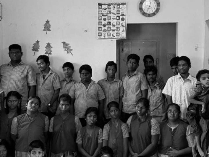 Group of school children and staff posing in a classroom with yellow walls.