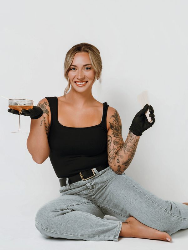 Smiling woman with tattoos, wearing black gloves, holding a drink and a fan.