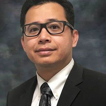 Professional man in suit and glasses posing against a dark background.
