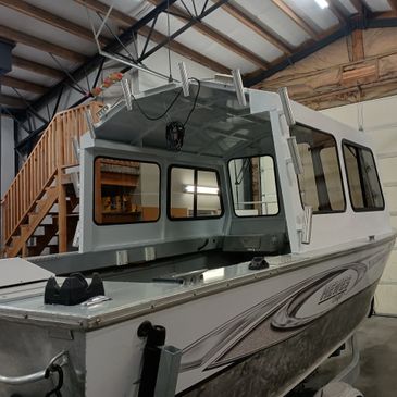 A white and silver boat with a cabin, stored indoors near wooden stairs.
