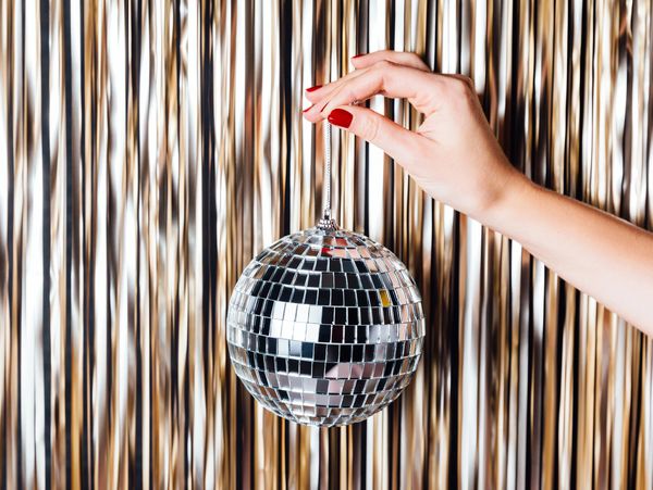 Woman hand is holding disco ball in the middle of Golden foil tinsel strips
