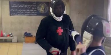 Two individuals sparring in a fencing practice indoors.