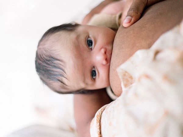Newborn baby breastfeeding, close-up of eyes and face.
