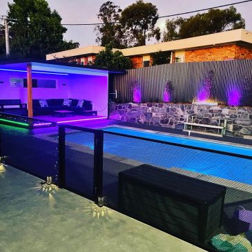 Modern backyard with illuminated pool and seating area at dusk.