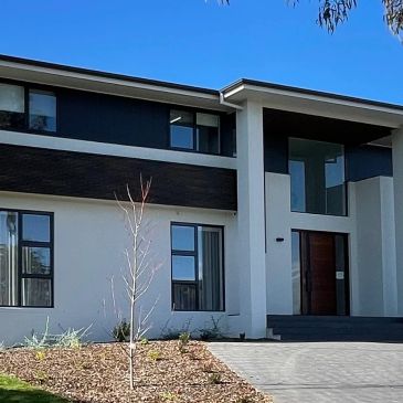 Modern house exterior with large windows and a clear sky.