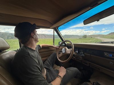 Man relaxing inside a vintage car, gazing out at a scenic countryside.