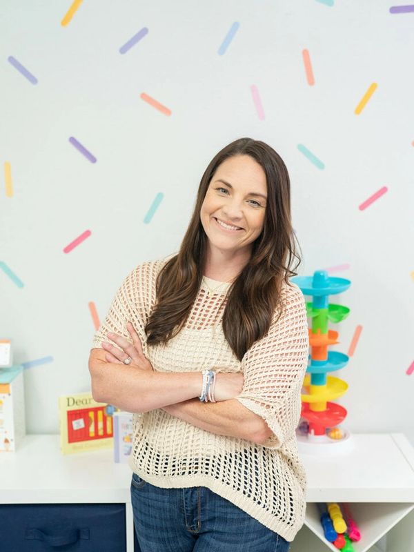 Smiling woman with crossed arms in a colorful, playful room.