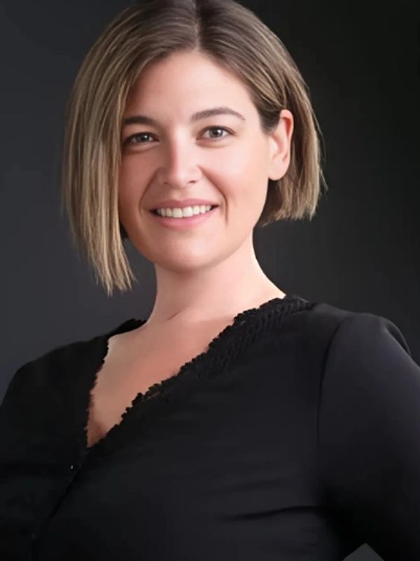 Young woman with short hair smiling against a dark background.