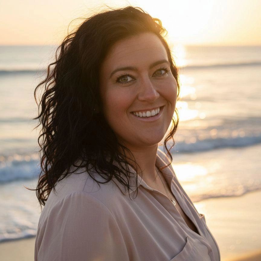 Smiling woman with curly hair at the beach during sunset.