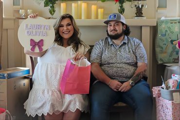 Couple celebrates with a personalized sign and gift bag in a cozy setting.