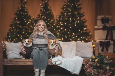 Woman sitting on a bench with two dogs in festive Christmas setting.