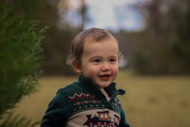A toddler smiles outdoors wearing a patterned sweater.