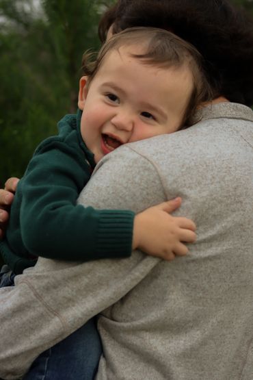 A happy toddler hugging an adult warmly outdoors.
