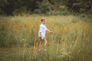 A young boy walking through a grassy field on a sunny day.