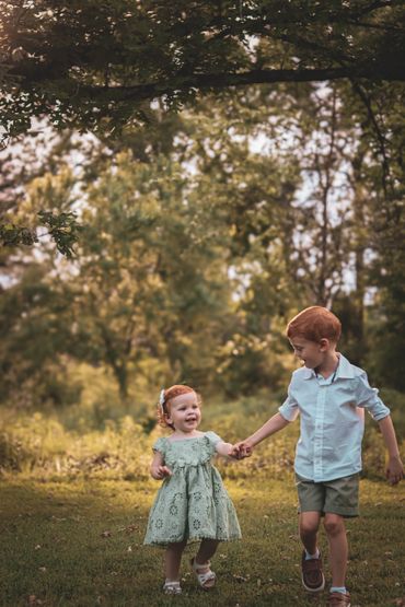 Two children holding hands and walking outdoors on a sunny day.