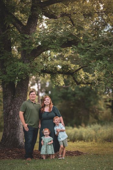 A family of four posing under a large tree outdoors.