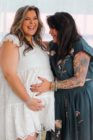 Two women share a joyful moment with one embracing the other's baby bump.