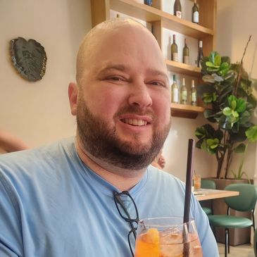 A smiling man in a blue shirt holding a cocktail in a cafe.