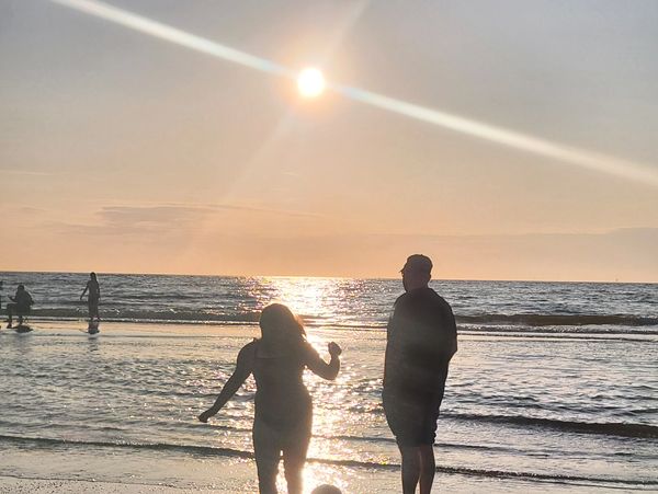 Silhouettes of two people enjoying a sunset at the beach.