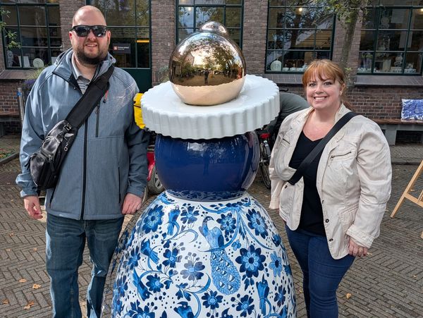Two people pose beside a large blue and white ceramic sculpture outdoors.