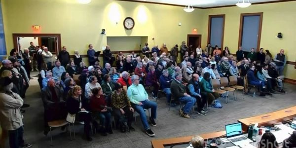 A large group attentively listens in a community meeting room.