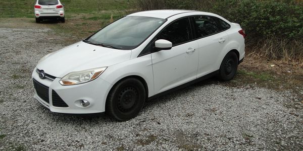 White Ford sedan parked on gravel near bushes.
