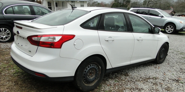 White Ford Focus sedan parked on gravel with other vehicles nearby.