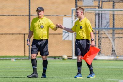 Two soccer referees fist bump on the field during a daytime game.