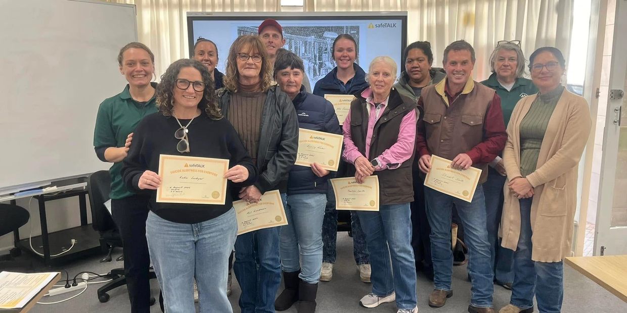 Group of people proudly holding certificates in a classroom setting.