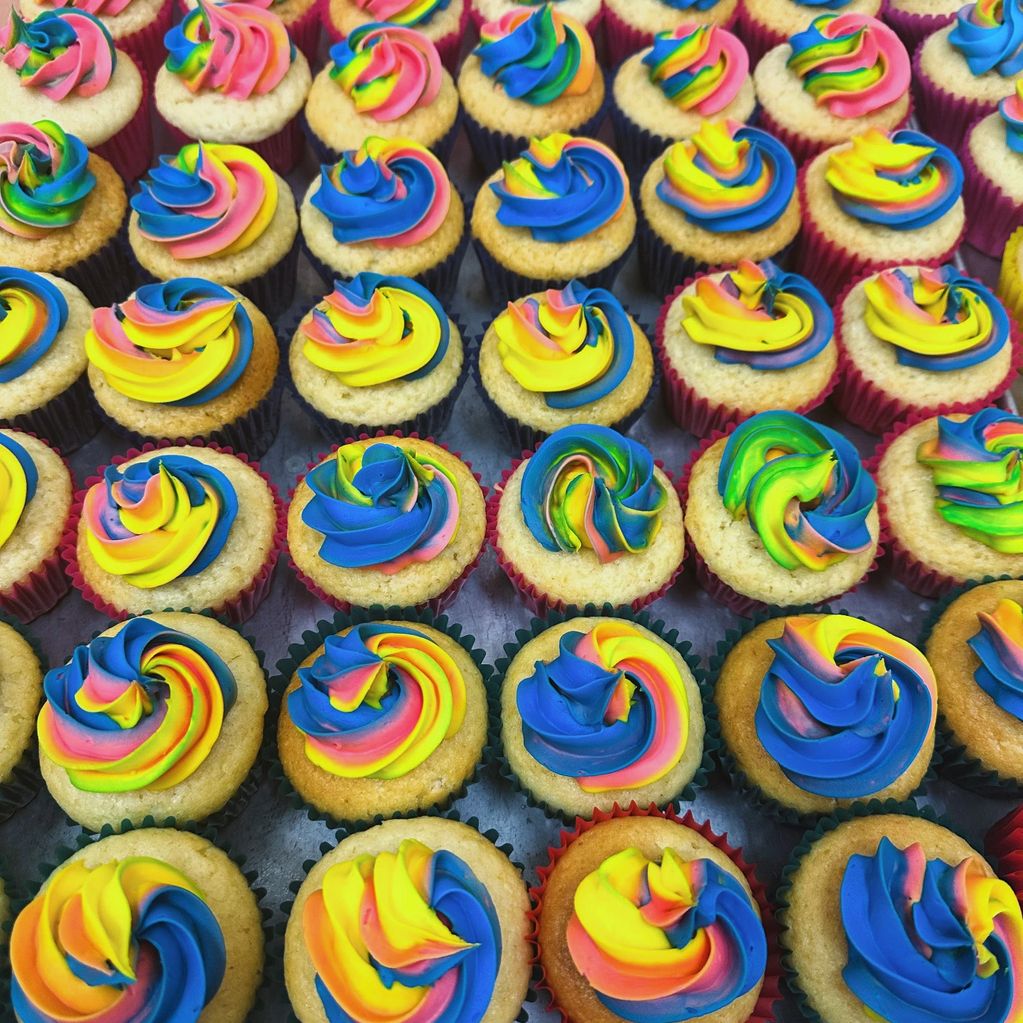 Cupcakes with vibrant rainbow swirl frosting in neat rows.