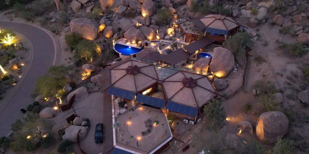 Aerial view of a uniquely designed desert home illuminated at dusk.