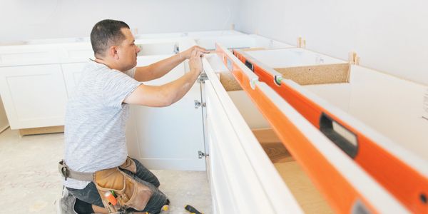 A man installs kitchen cabinets using a level tool.