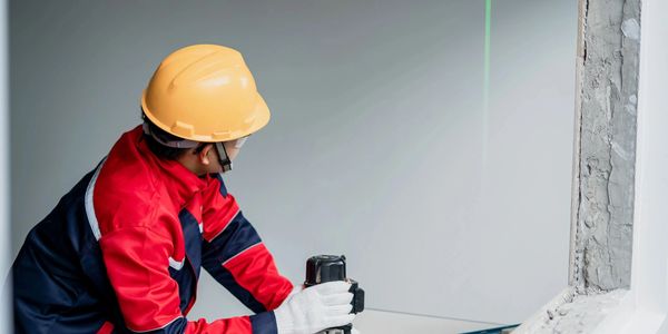 Worker in safety gear using a laser level indoors.