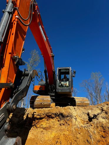 Excavator working on a dirt excavation under clear blue sky.