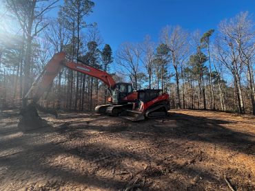 Excavator parked on cleared land in forest area.