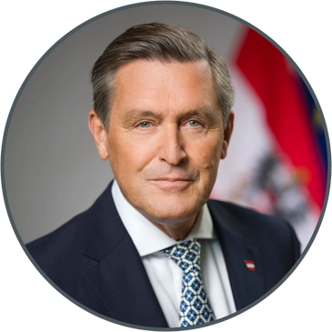 Professional portrait of a man in a suit with a flag background.