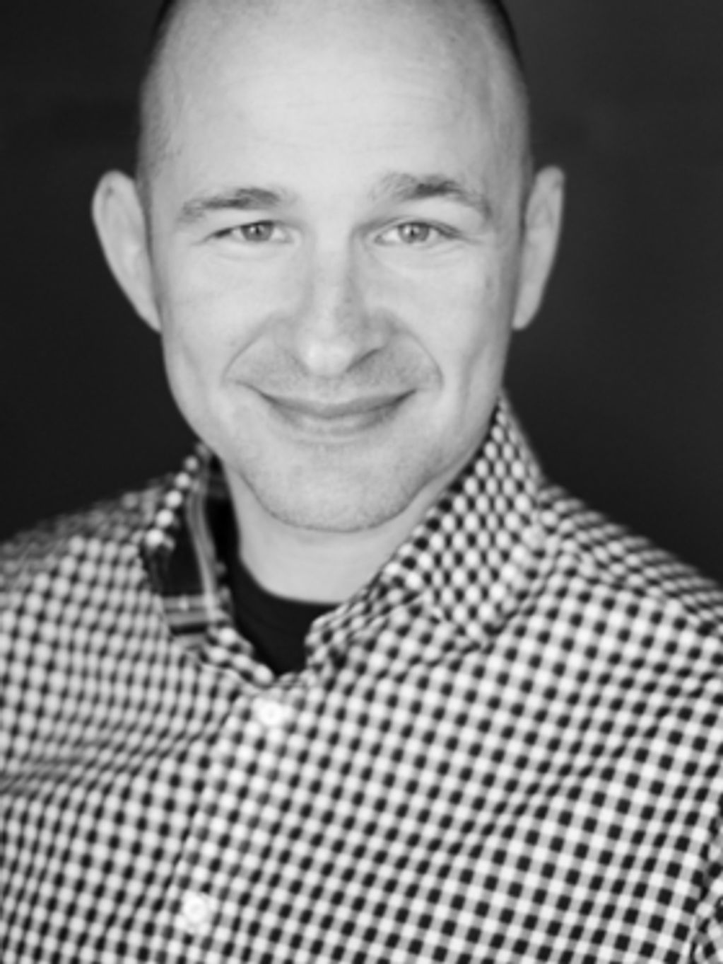 Smiling man in checkered shirt.
