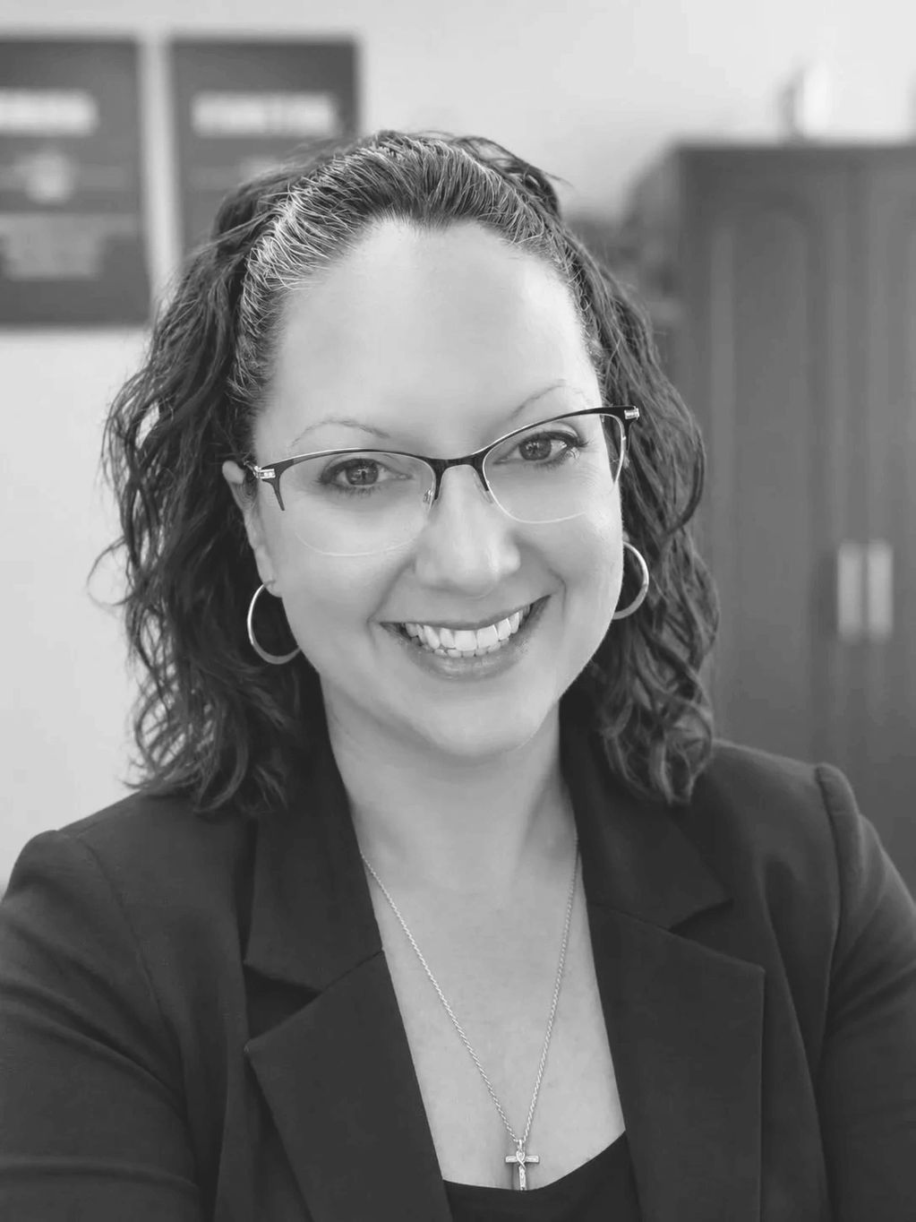 Smiling woman with glasses and curly hair in a blazer.