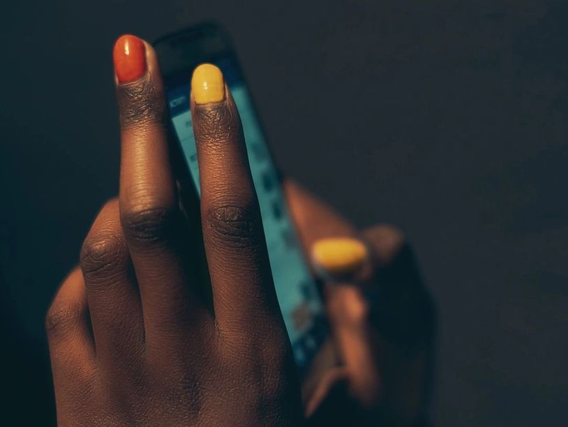 Hand with orange and yellow painted nails holding a smartphone.