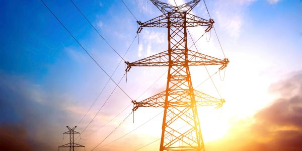 High voltage power lines against a bright sky at sunset.