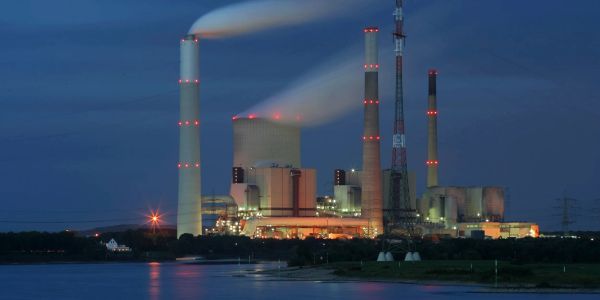 A power plant emitting smoke at night by the water.