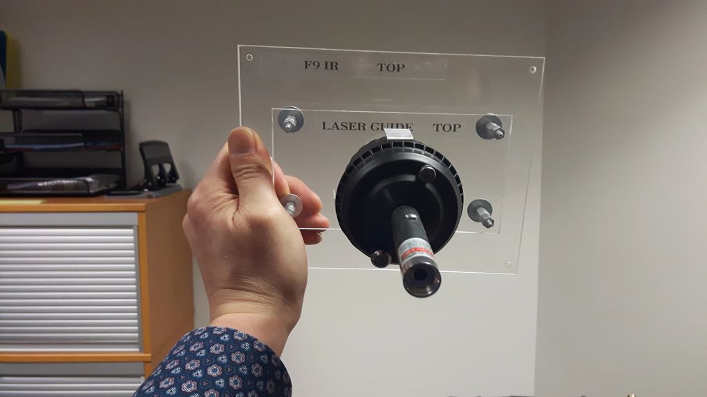 Hand holding a laser guide apparatus with labeled transparent panel.