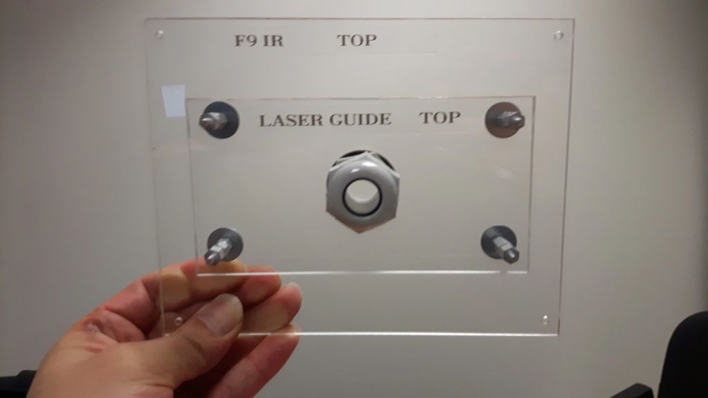 Hand holding a transparent plastic guide labeled for laser and F9 IR top alignment.