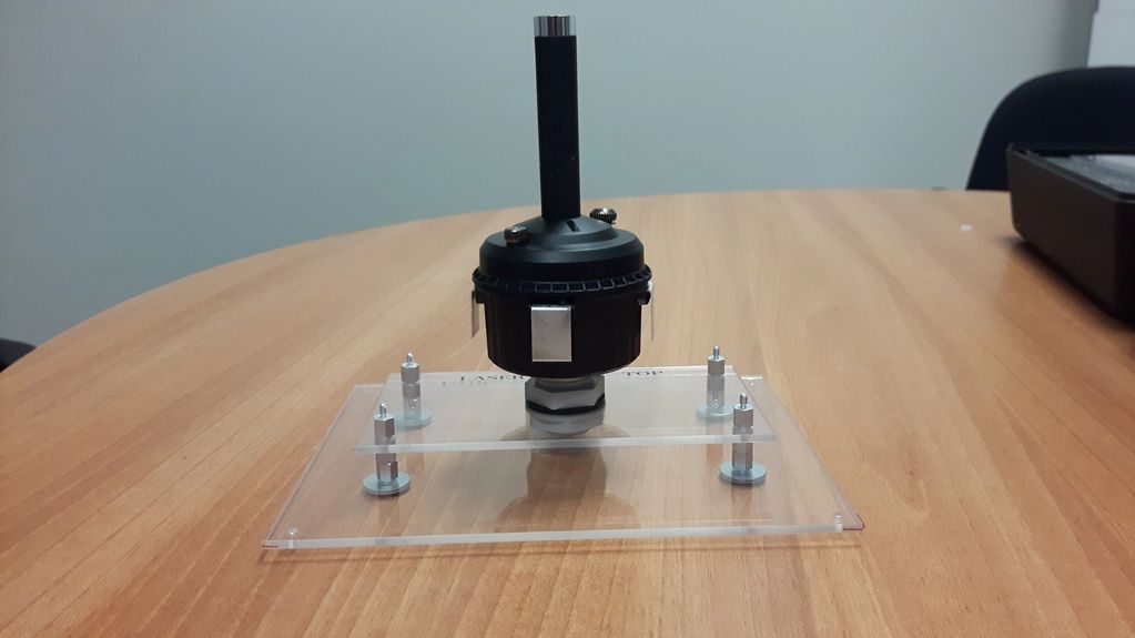 A black device mounted on a transparent stand on a wooden table.