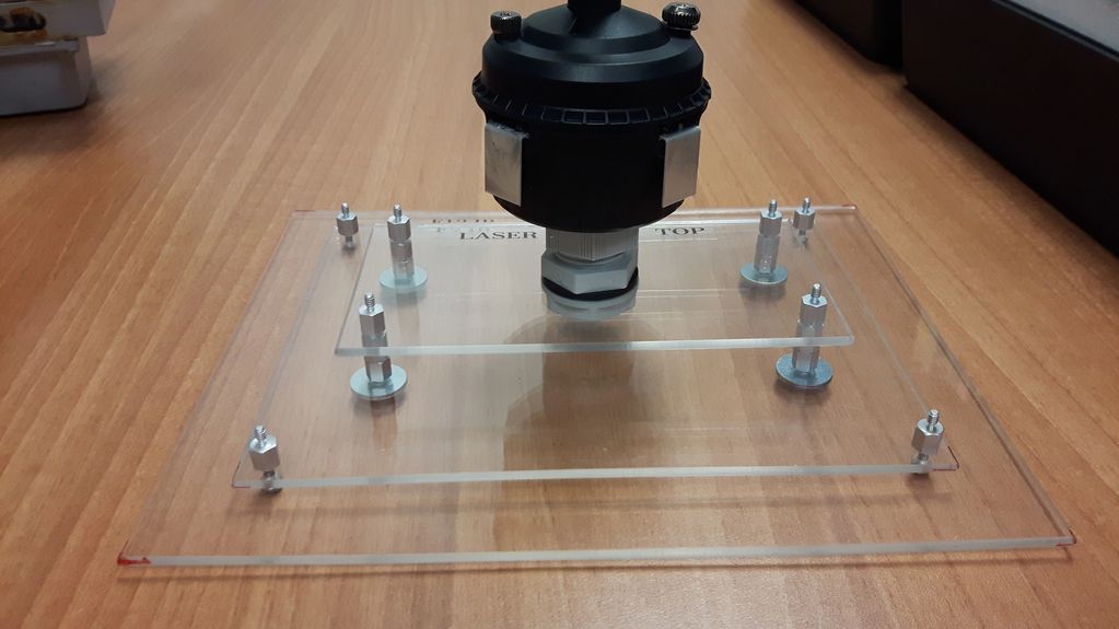 A laser engraving setup with clear acrylic plates and metal fasteners on a wooden table.