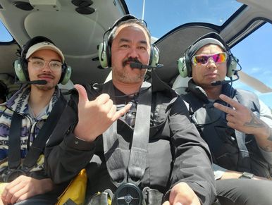 Three men wearing headsets inside a helicopter cockpit.